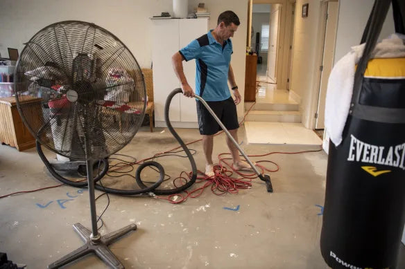 Man using a vacuum cleaner on floor during restoration with a large fan and punching bag nearby