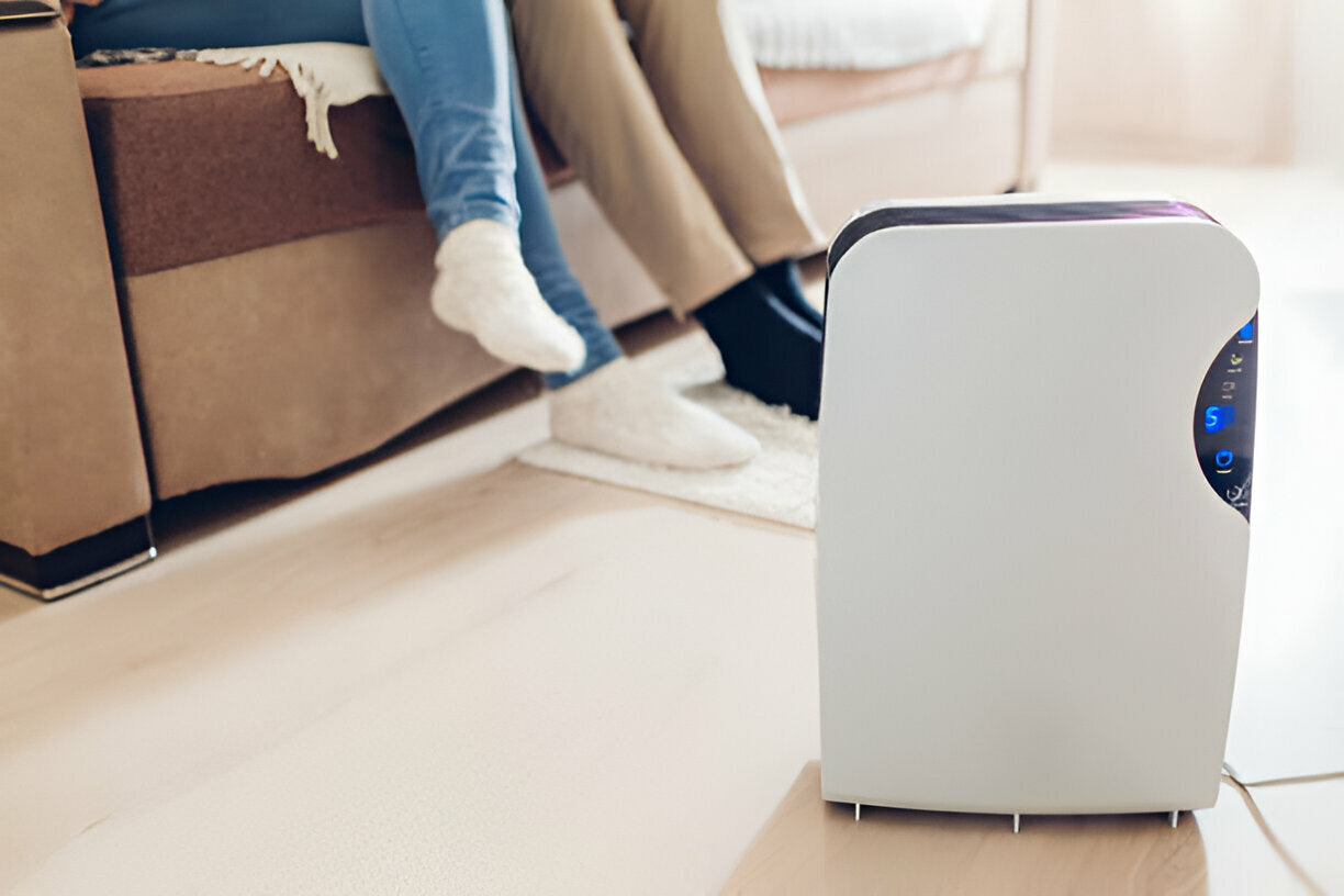 Modern air purifier placed on the floor near a couch with two people sitting and relaxing