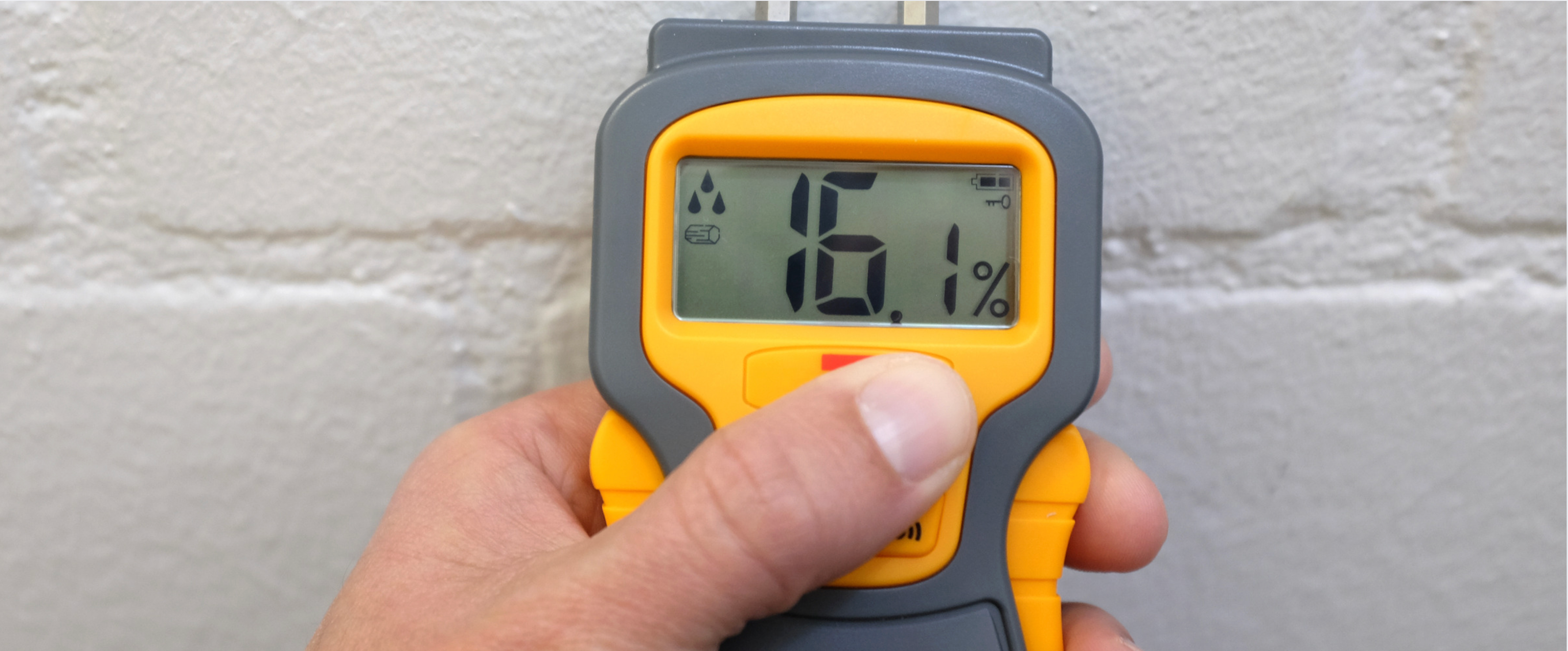 Hand holding moisture meter showing 16.1 percent reading on wall for water damage restoration assessment